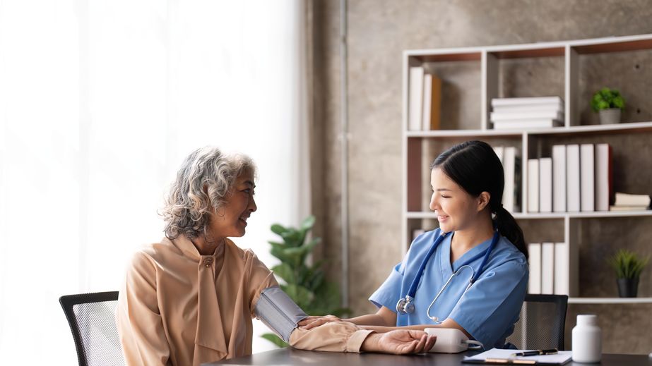 A nurse in blue scrubs is taking the blood pressure of an older woman in an office setting.